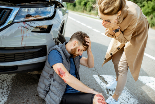 injured man suffering on the pedestrian crossing near the car after the road accident