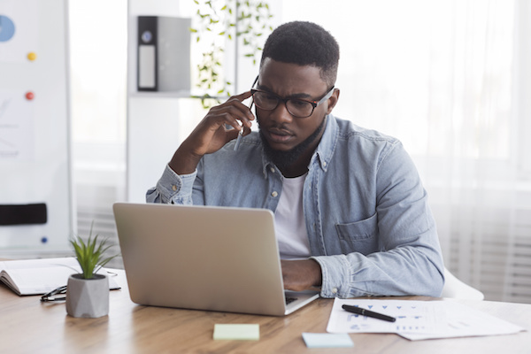 Man talks on phone while looking at laptop screen